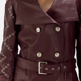 A stylish woman wearing a maroon leather trench coat, looking confident and fashionable.